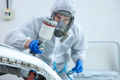 Photo of Worker painting car in body shop, selective focus