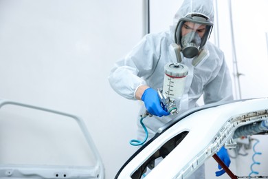 Photo of Worker spray painting car in body shop. Space for text