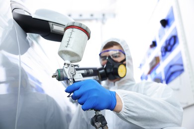 Photo of Worker painting car in body shop, selective focus
