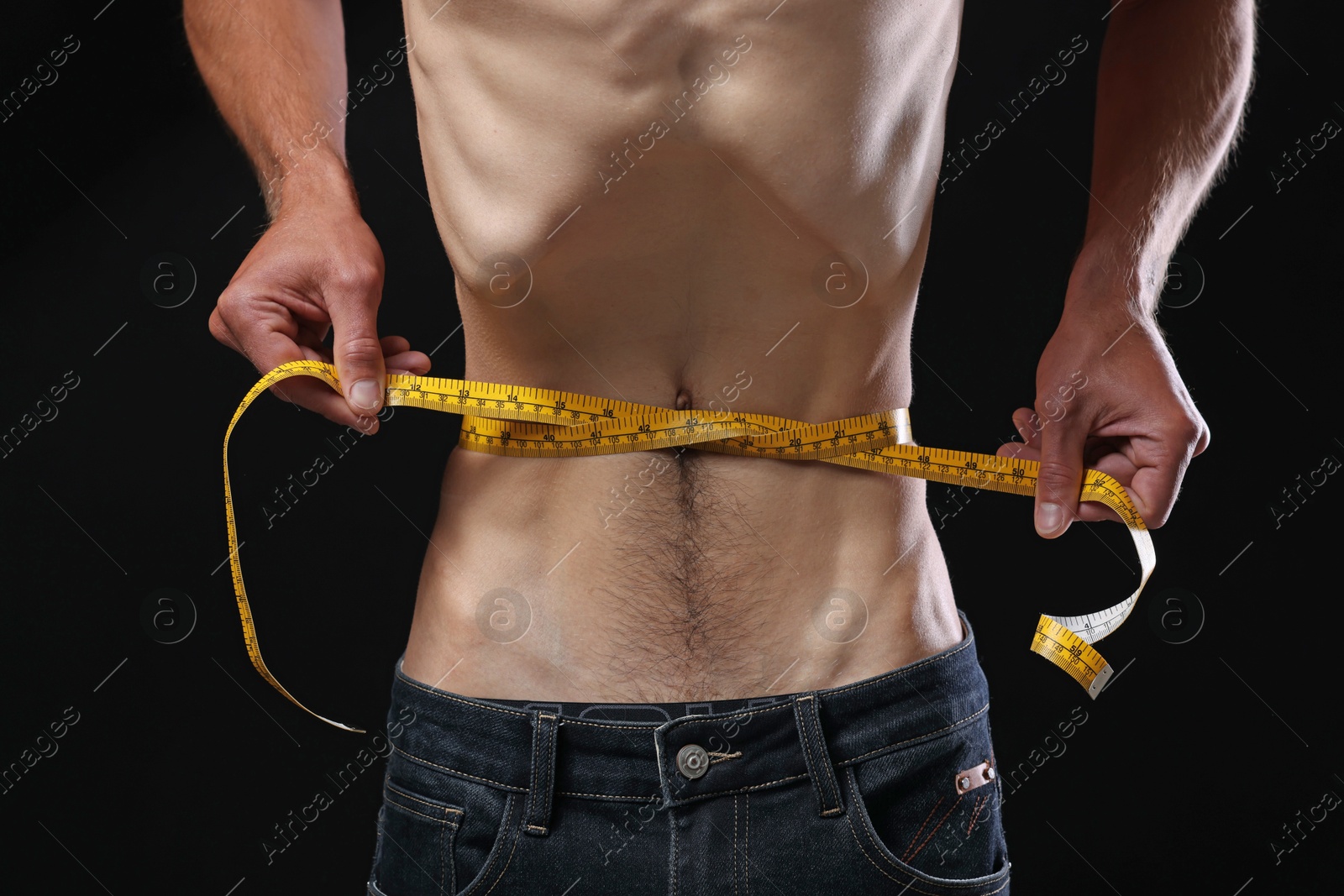 Anorexic man measuring his waist on black background, closeup Photo of Anorexic man measuring his waist on black background, closeup