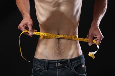 Photo of Anorexic man measuring his waist on black background, closeup
