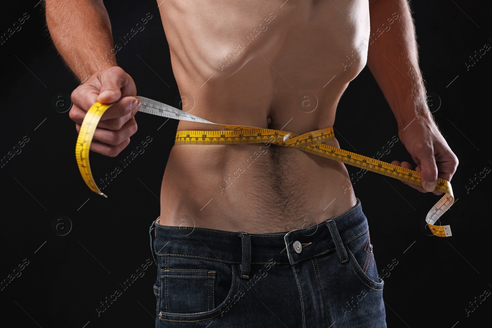 Anorexic man measuring his waist on black background, closeup Photo of Anorexic man measuring his waist on black background, closeup