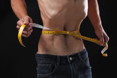 Photo of Anorexic man measuring his waist on black background, closeup