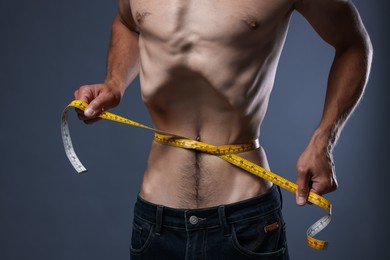 Photo of Anorexic man measuring his waist on grey background, closeup