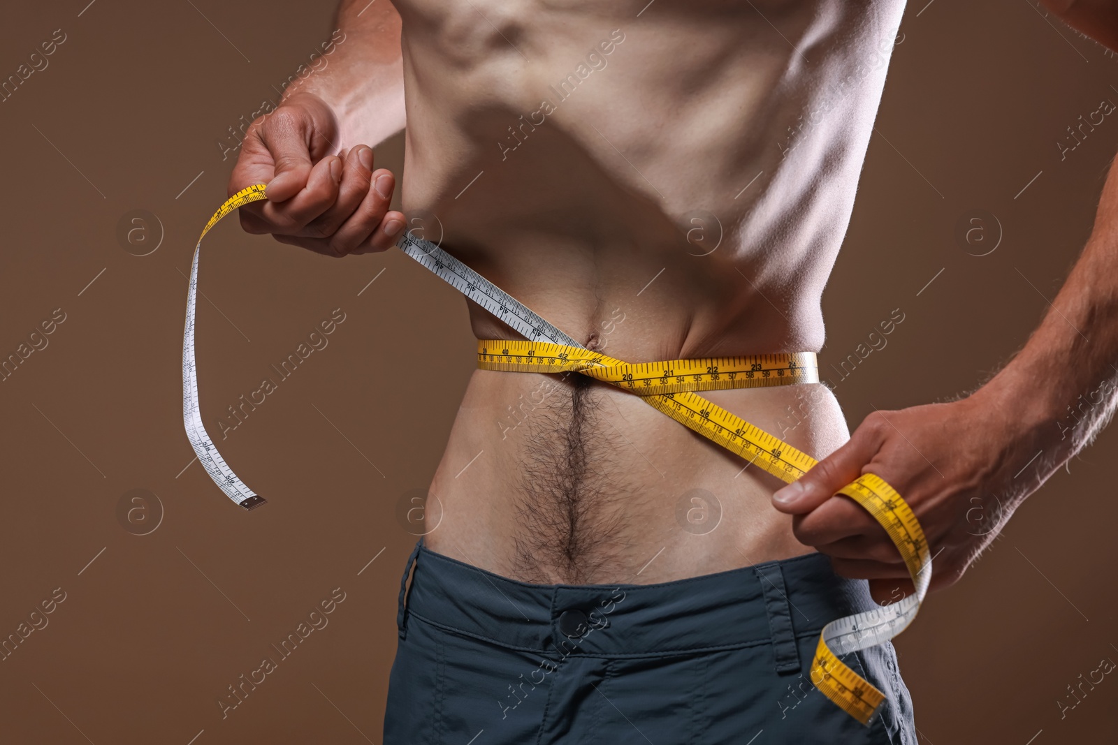 Anorexic man measuring his waist on beige background, closeup Photo of Anorexic man measuring his waist on beige background, closeup