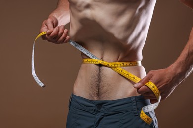 Photo of Anorexic man measuring his waist on beige background, closeup