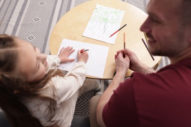 Photo of Father teaching his daughter to draw at table indoors, above view