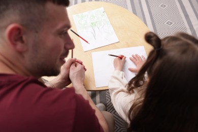 Photo of Father teaching his daughter to draw at table indoors, above view