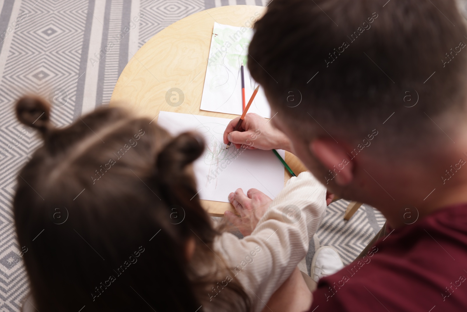 Father teaching his daughter to draw at table indoors, above view Photo of Father teaching his daughter to draw at table indoors, above view