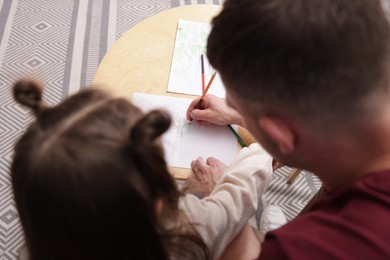 Photo of Father teaching his daughter to draw at table indoors, above view