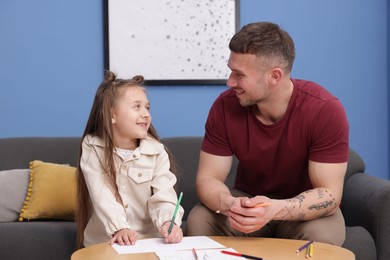Photo of Father teaching his daughter to draw at table indoors