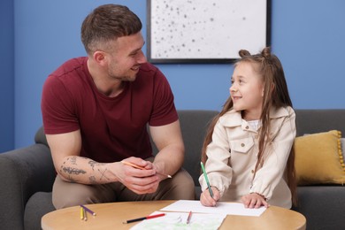 Photo of Father teaching his daughter to draw at table indoors