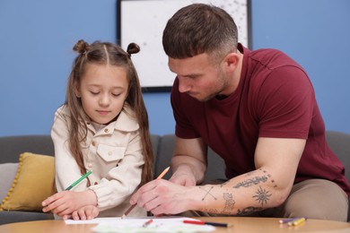 Photo of Father teaching his daughter to draw at table indoors