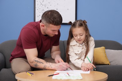 Photo of Father teaching his daughter to draw at table indoors