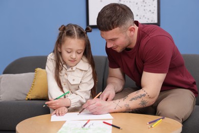 Photo of Father teaching his daughter to draw at table indoors