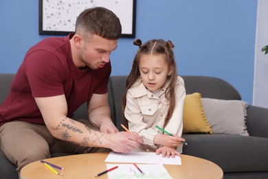 Photo of Father teaching his daughter to draw at table indoors
