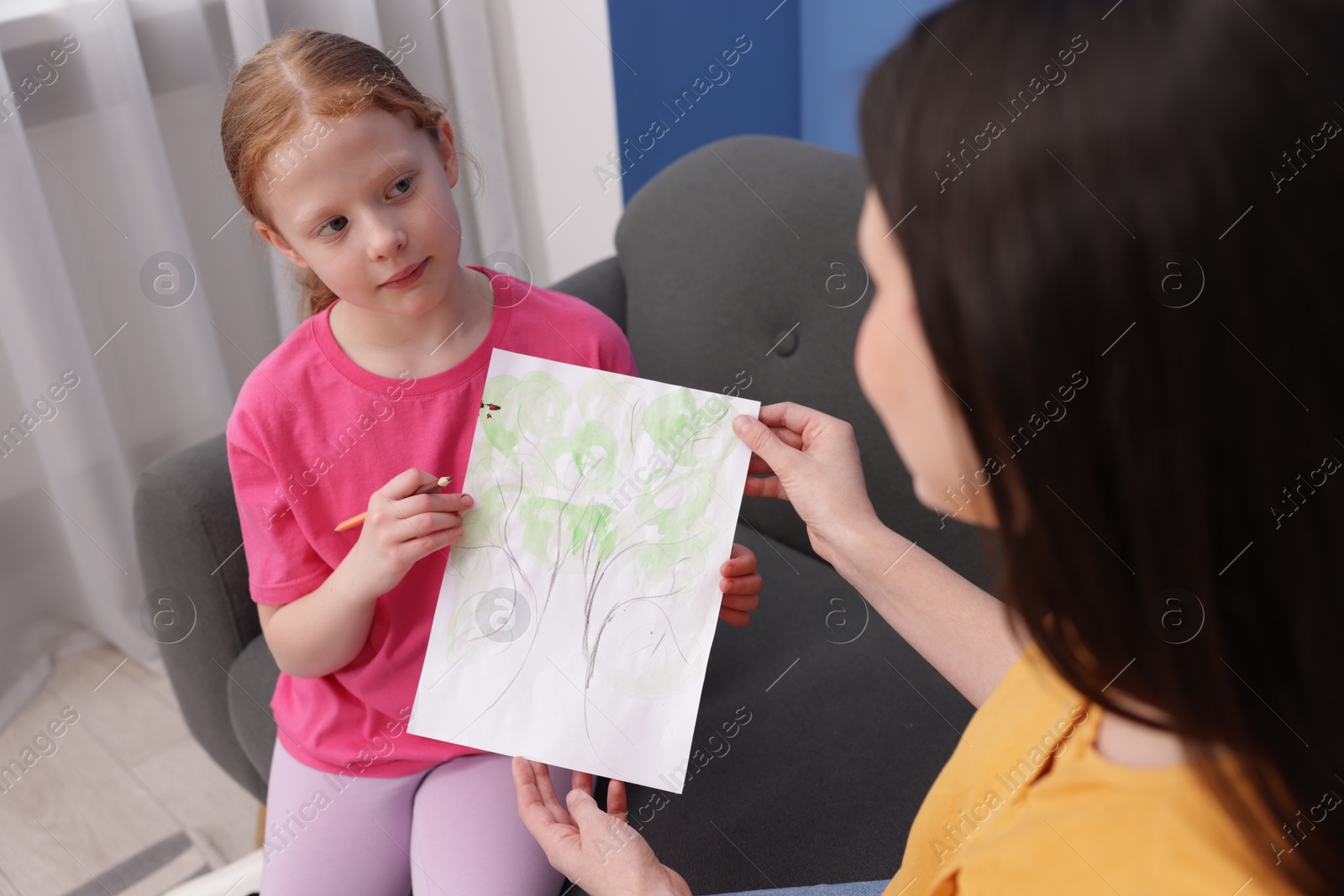 Cute girl showing her mother drawing on sofa at home Photo of Cute girl showing her mother drawing on sofa at home