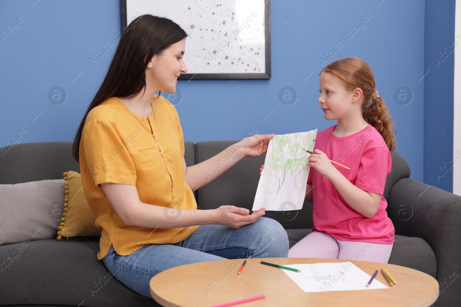 Cute girl showing her mother drawing on sofa at home Photo of Cute girl showing her mother drawing on sofa at home
