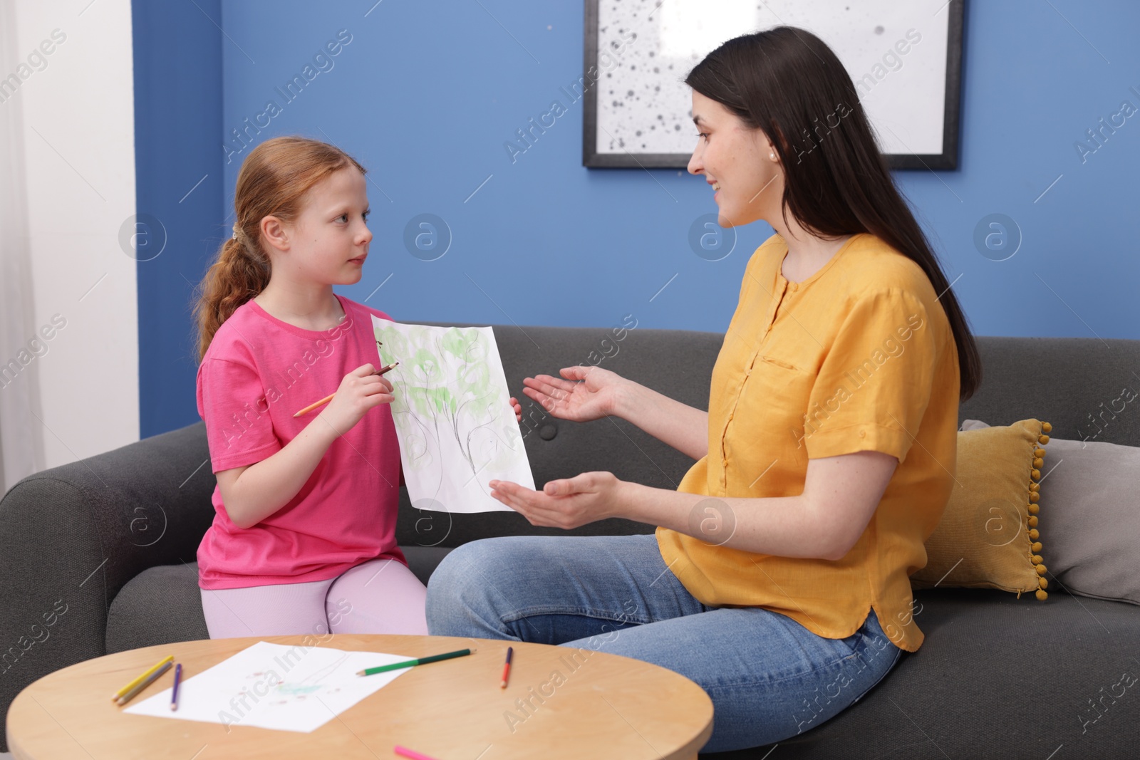 Cute girl showing her mother drawing on sofa at home Photo of Cute girl showing her mother drawing on sofa at home