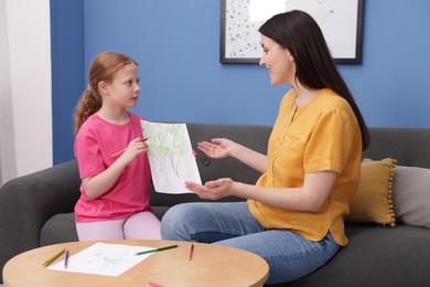Photo of Cute girl showing her mother drawing on sofa at home