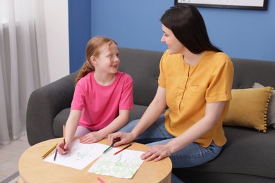 Photo of Mother teaching her daughter to draw at table indoors