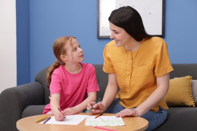 Photo of Mother teaching her daughter to draw at table indoors