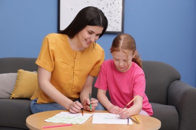 Photo of Mother teaching her daughter to draw at table indoors