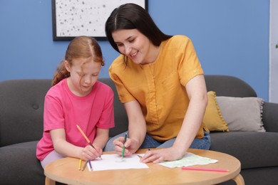 Photo of Mother teaching her daughter to draw at table indoors