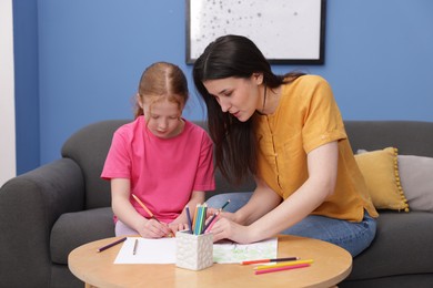 Photo of Mother teaching her daughter to draw at table indoors