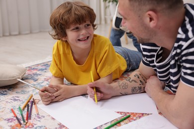 Photo of Father teaching his son to draw on floor at home