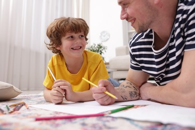 Photo of Father teaching his son to draw on floor at home, closeup