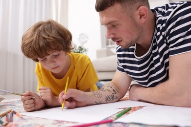 Photo of Father teaching his son to draw on floor at home