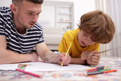 Photo of Father teaching his son to draw on floor at home
