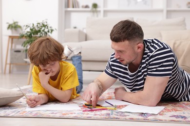 Photo of Father teaching his son to draw on floor at home