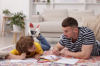 Photo of Father teaching his son to draw on floor at home