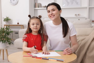 Photo of Mother teaching her daughter to draw at table indoors