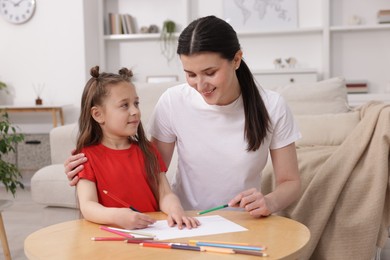 Photo of Mother teaching her daughter to draw at table indoors