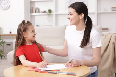 Photo of Mother teaching her daughter to draw at table indoors