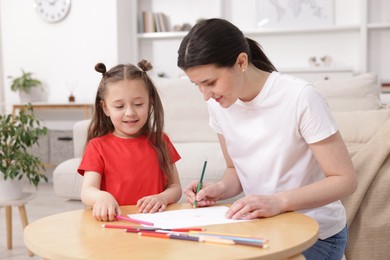 Photo of Mother teaching her daughter to draw at table indoors