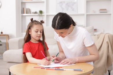 Photo of Mother teaching her daughter to draw at table indoors