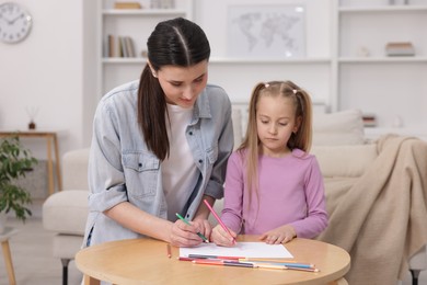 Photo of Mother teaching her daughter to draw at table indoors