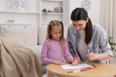 Photo of Mother teaching her daughter to draw at table indoors, space for text