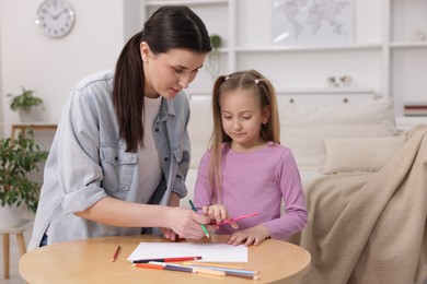 Photo of Mother teaching her daughter to draw at table indoors, space for text