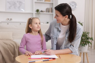 Photo of Mother teaching her daughter to draw at table indoors