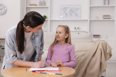 Photo of Mother teaching her daughter to draw at table indoors, space for text