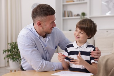Photo of Father teaching his son to draw at table indoors