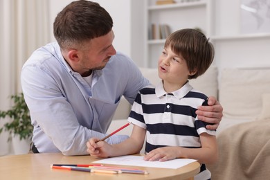 Photo of Father teaching his son to draw at table indoors