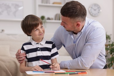 Photo of Father teaching his son to draw at table indoors