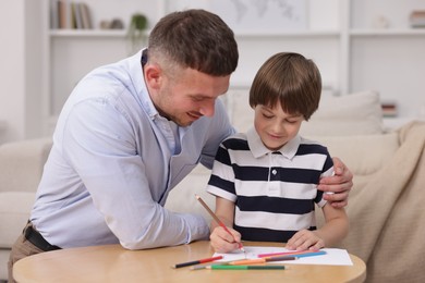 Photo of Father teaching his son to draw at table indoors