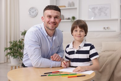 Photo of Father teaching his son to draw at table indoors